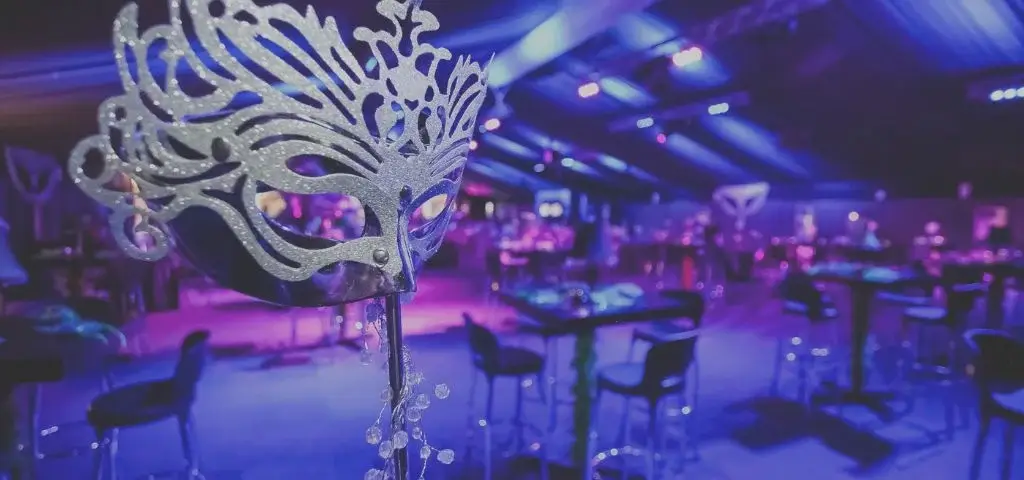 Gala event venue lit in purple with a masquerade mask in the foreground